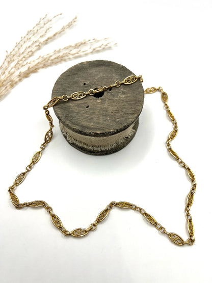 A yellow gold fancy link chain lying on a wooden object, on a white background