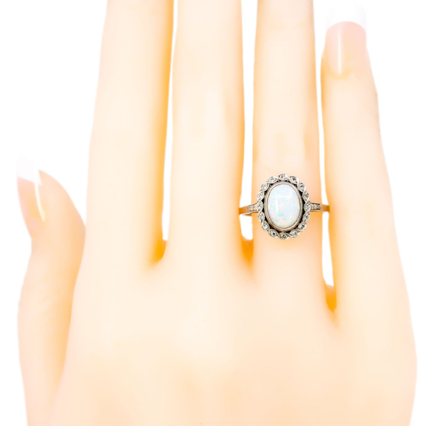 An oval opal and diamond cluster ring in platinum, modelled on a hand