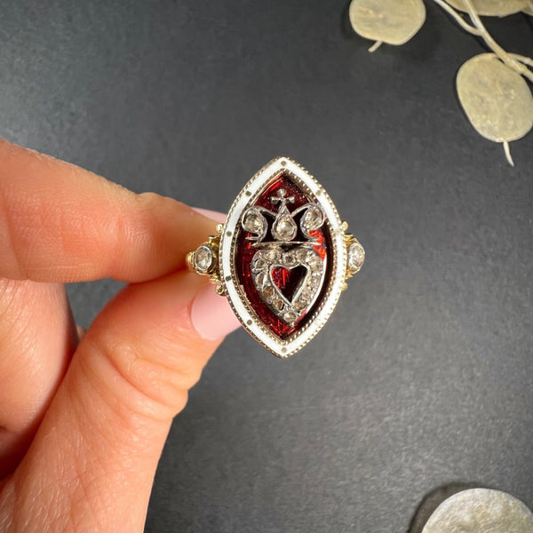 An ornate diamond and enamel navette shaped antique ring, held in a hand