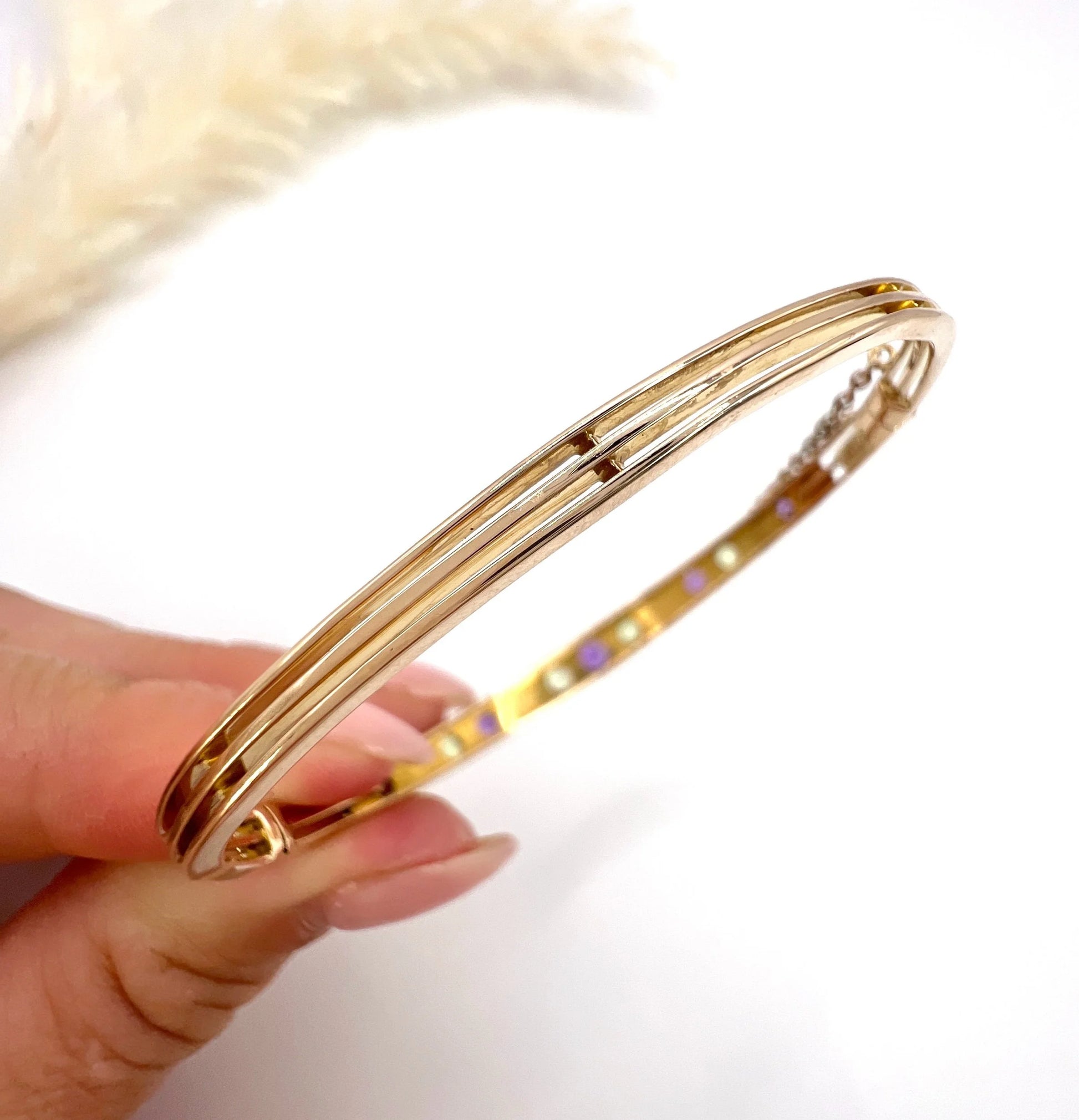 A yellow gold peridot, amethyst and pearl bangle bracelet, held in a hand