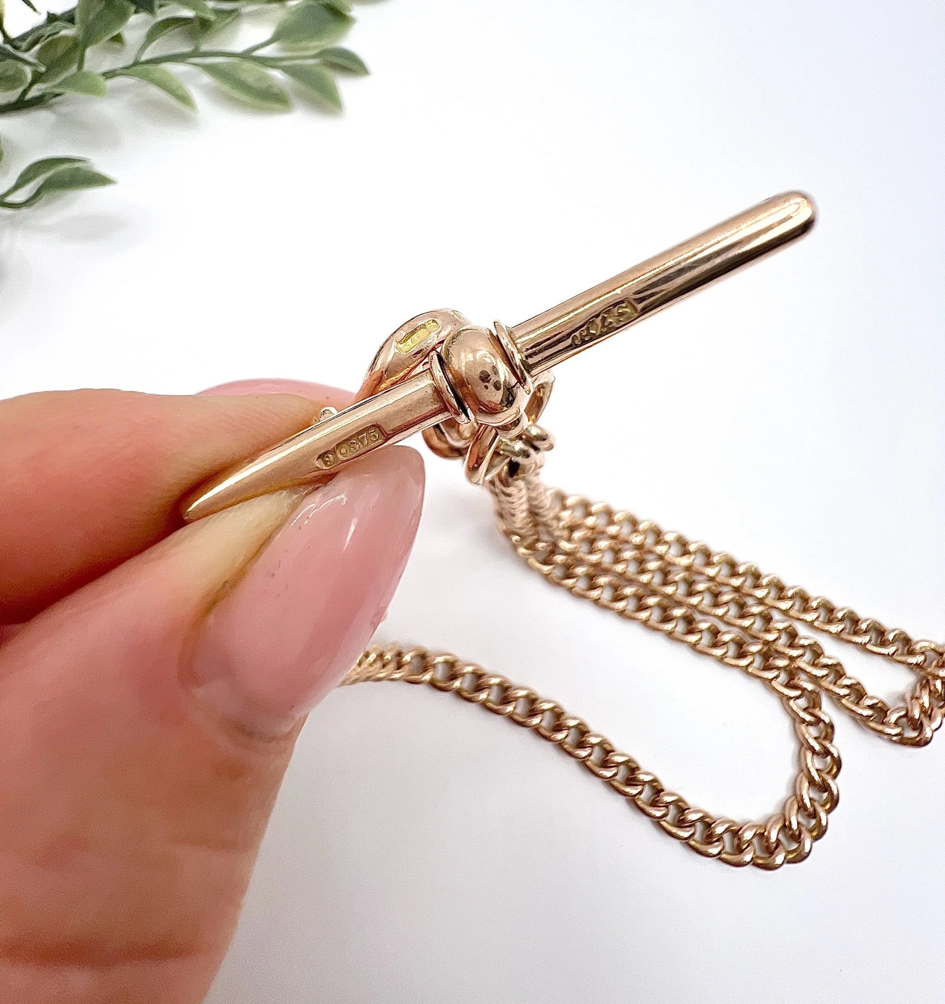 The t-bar of a gold curb link Albert chain, held in a hand