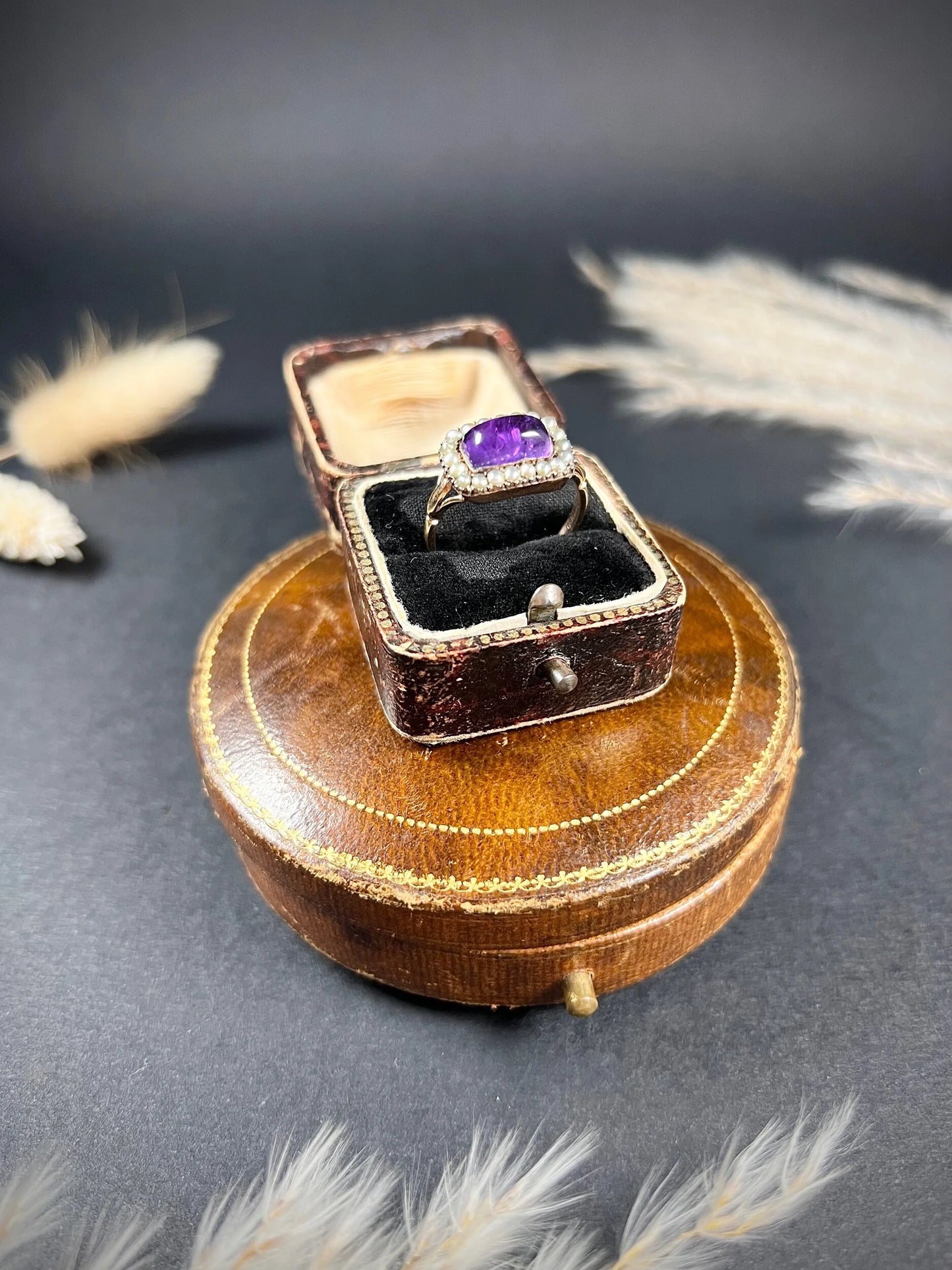 A cabochon amethyst and pearl halo cluster ring in gold, in a ring box