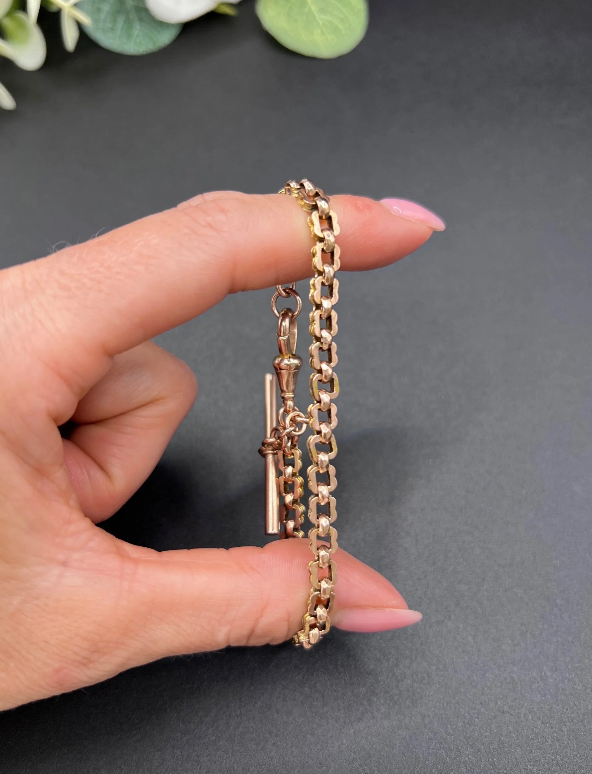 A fancy link rose gold bracelet with a T-bar and dog clip clasp, held in a hand
