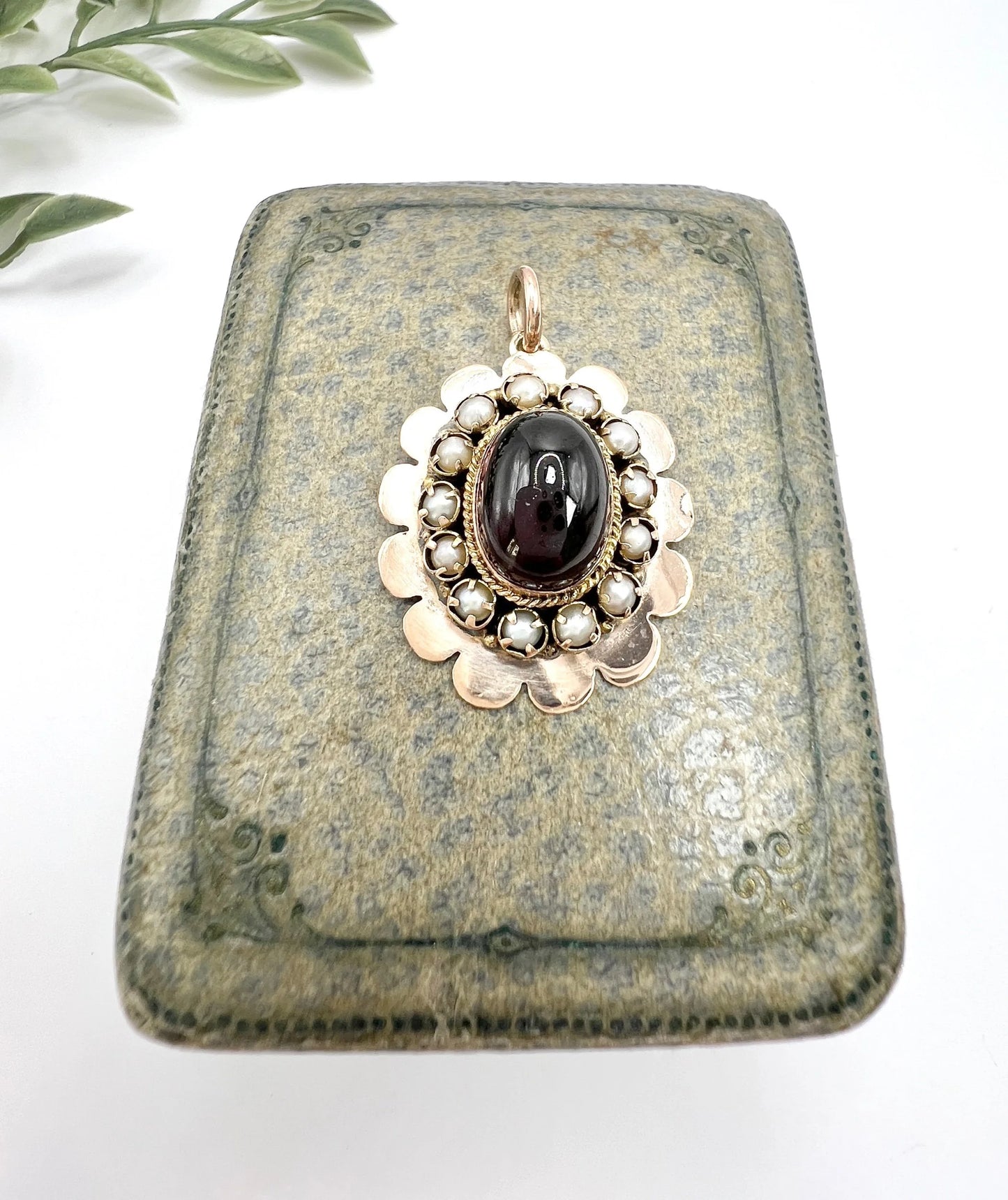 A cabochon garnet pendant with a seed pearl border in rose gold
