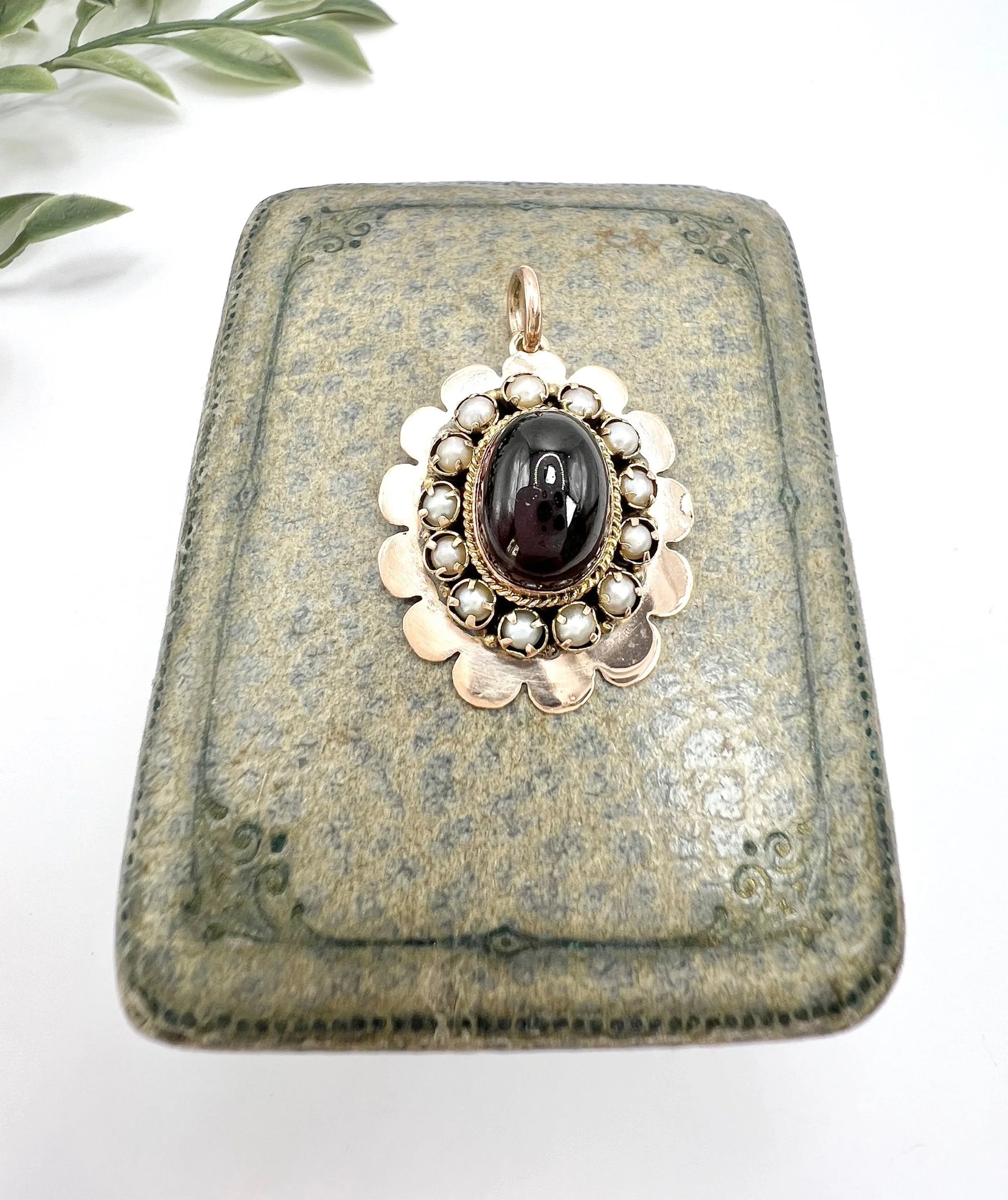 A cabochon garnet pendant with a seed pearl border in rose gold
