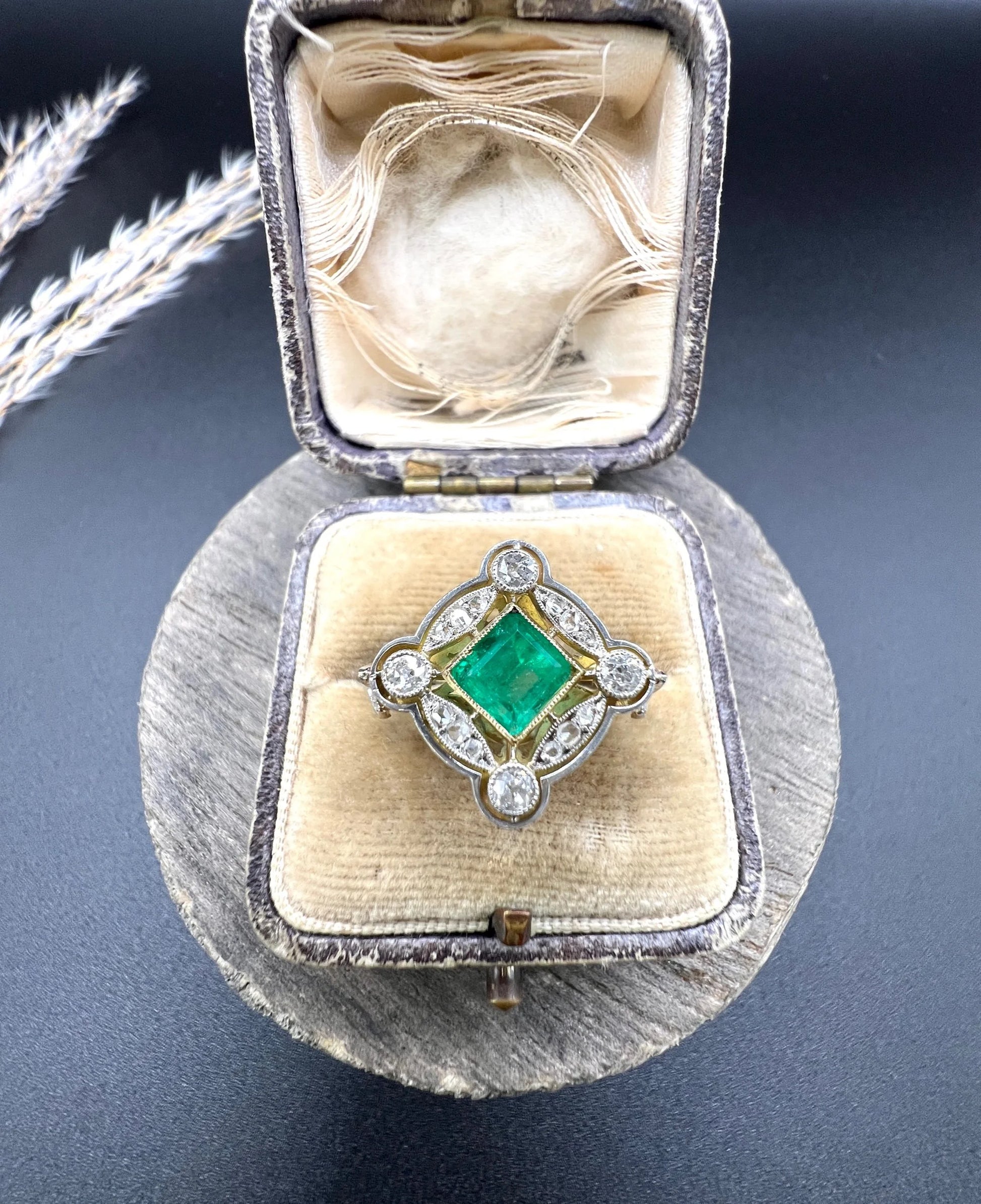 A gold and platinum ring with a centre emerald and diamond surround, in an antique ring box