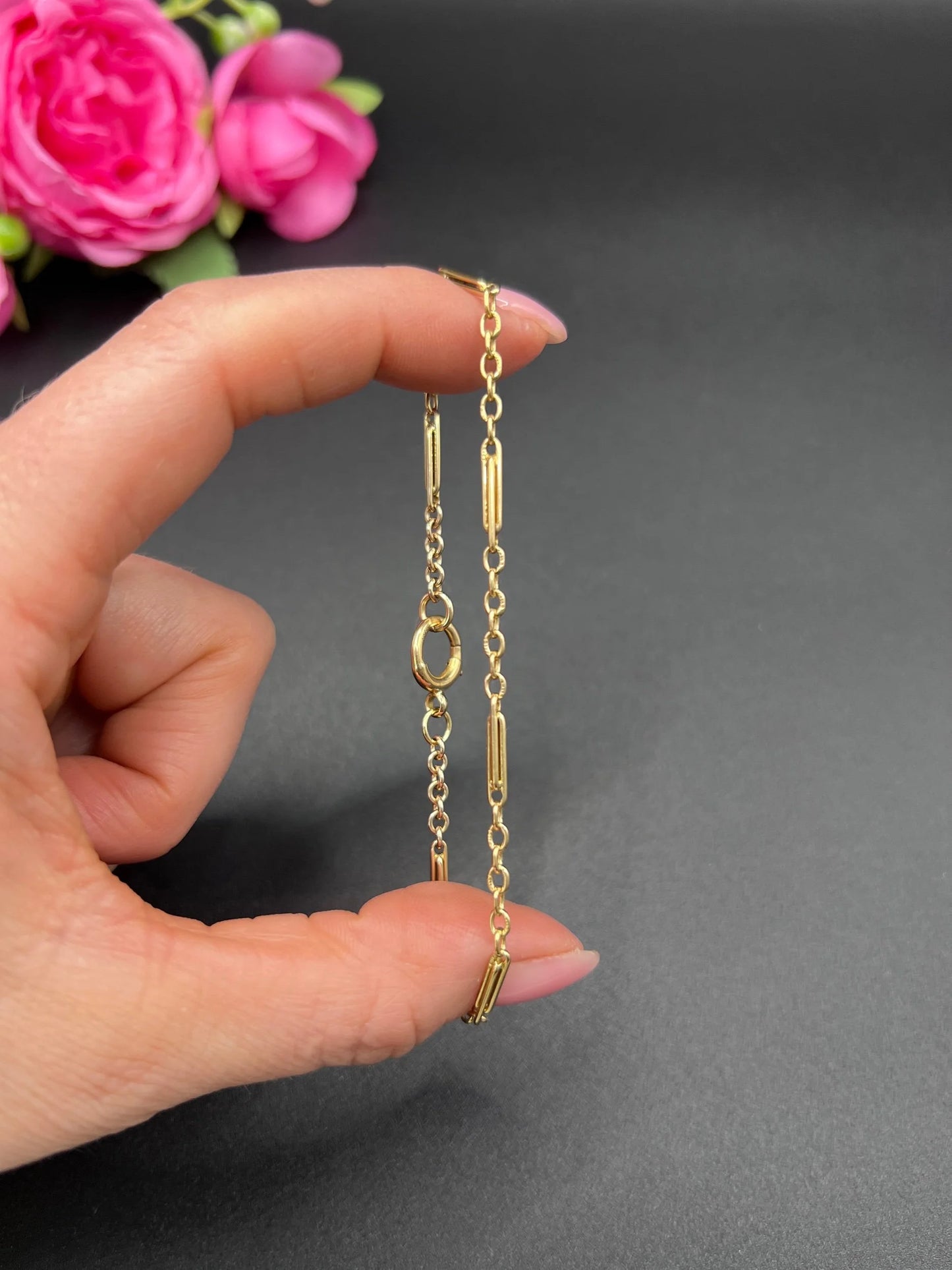 A yellow gold chain link bracelet with a bolt ring clasp, held in a hand