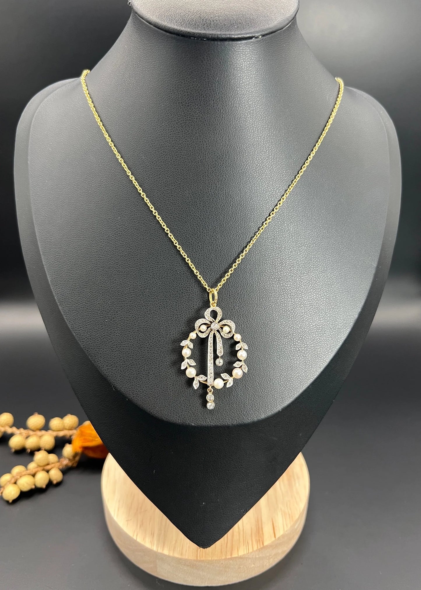 A pearl and diamond bow pendant in gold and platinum, with a chain, on a black bust