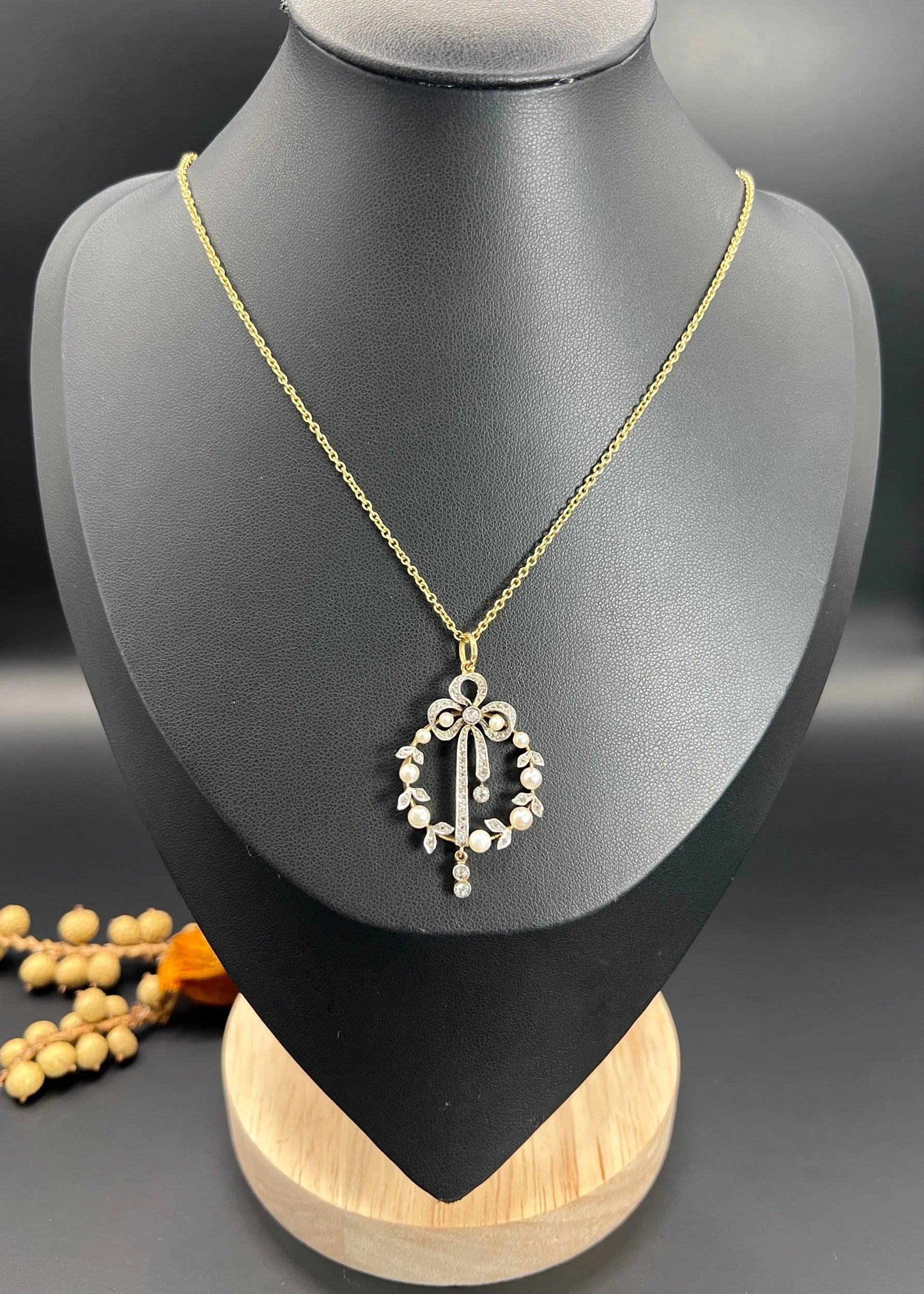 A pearl and diamond bow pendant in gold and platinum, with a chain, on a black bust