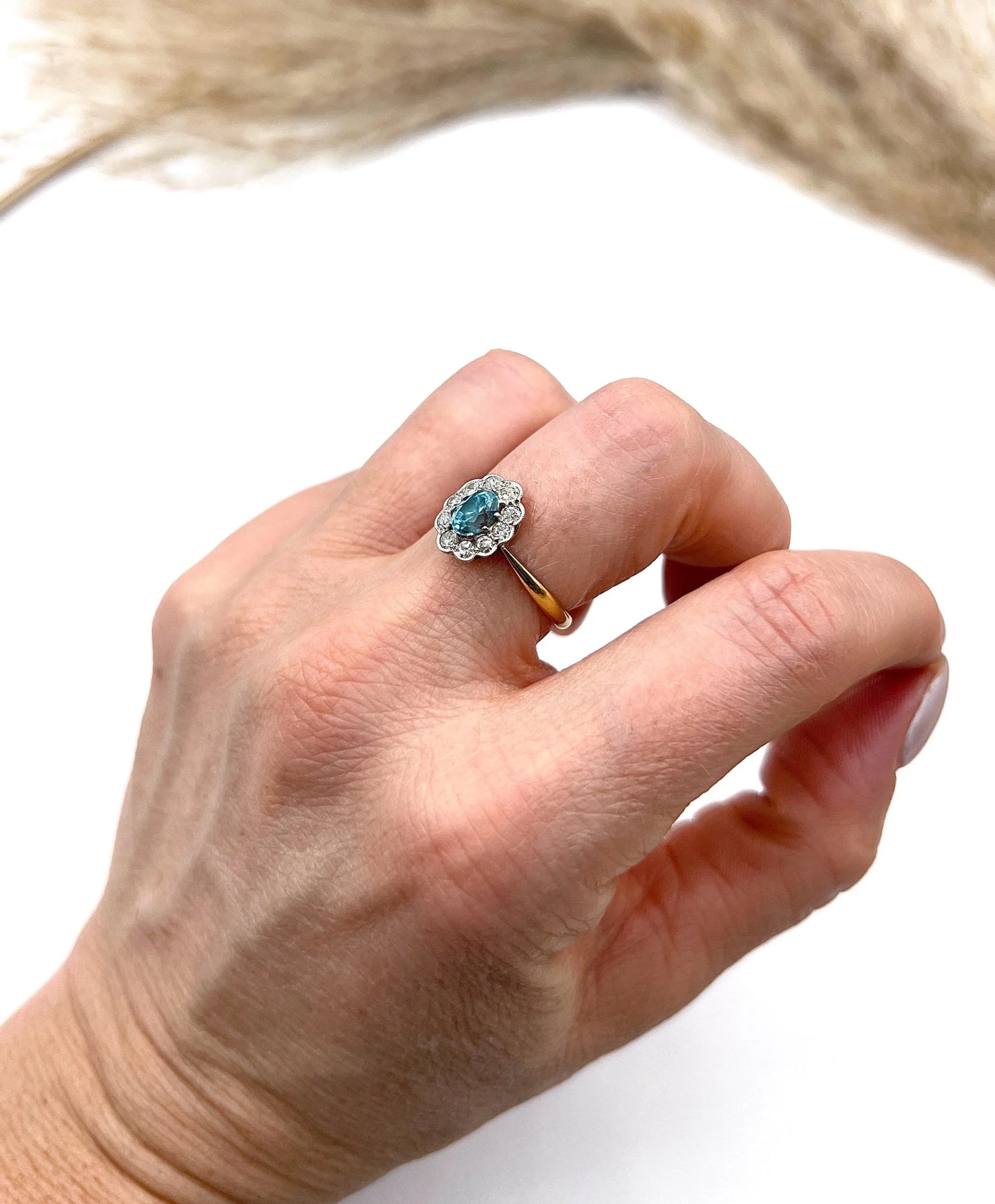 An oval cluster ring with a blue zircon centre surrounded by round diamonds, in yellow gold and platinum, modelled on a hand