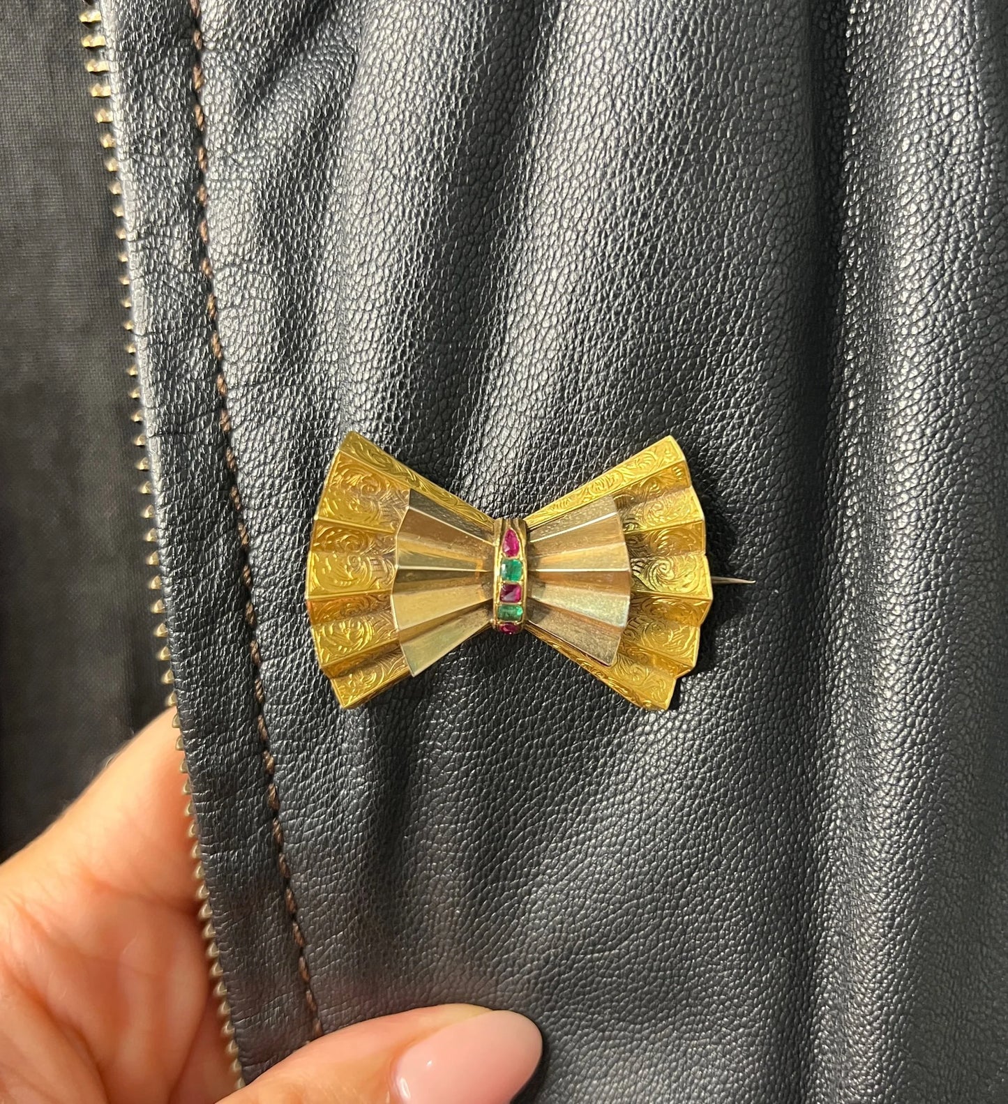 A yellow gold bow shaped brooch with rubies and emeralds, on a black jacket
