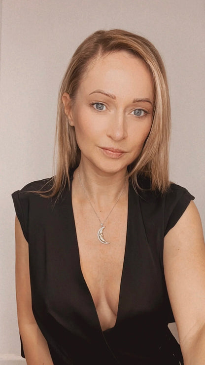 A gold crescent moon pendant with diamonds, on a chain, modelled by a woman wearing a black top