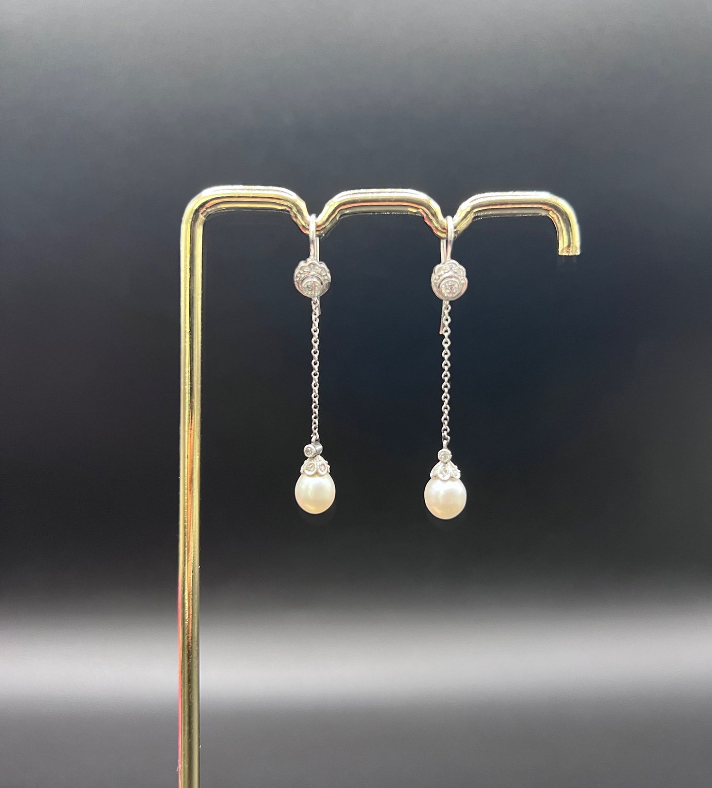 A pair of long drop platinum earrings with pearls and diamonds, on a gold hook