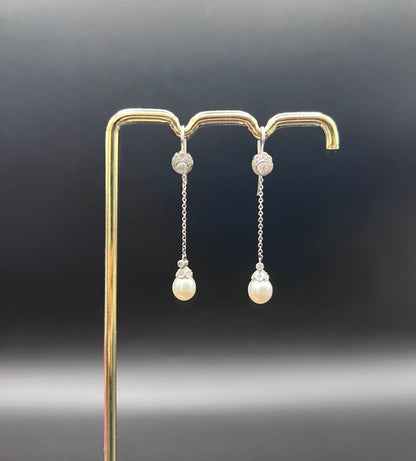 A pair of long drop platinum earrings with pearls and diamonds, on a gold hook