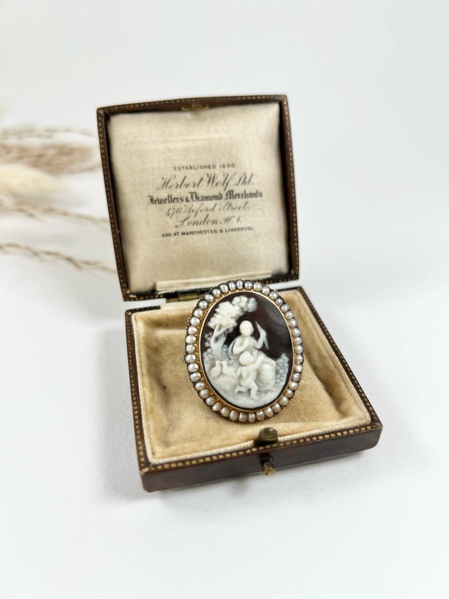 An antique oval cameo brooch depicting cherubs and birds, with a pearl border, set in gold
