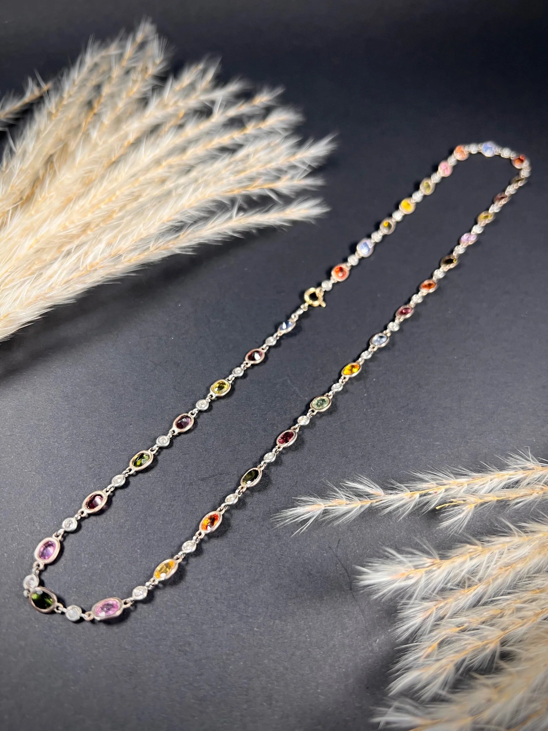 A coloured sapphire and diamond set necklace in platinum and gold, on a black background