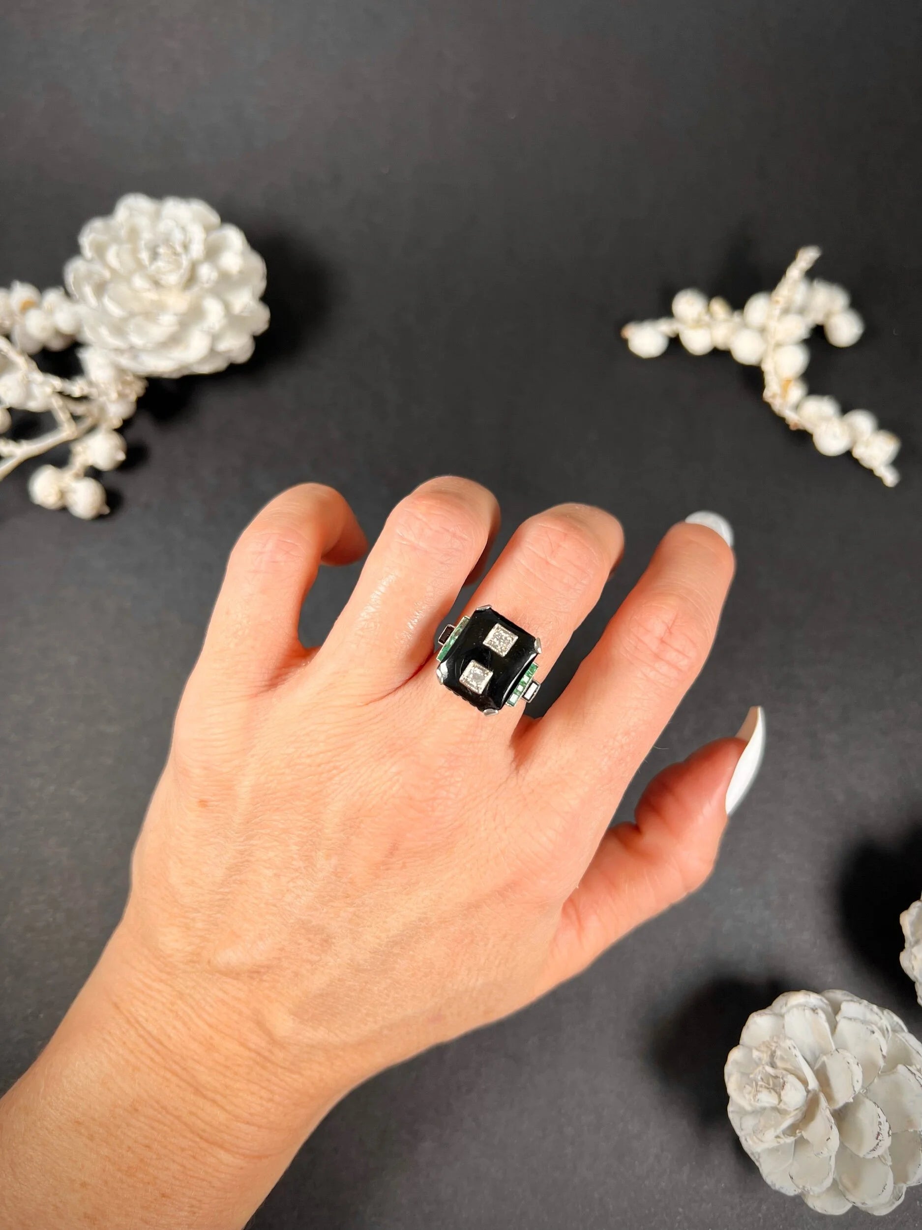 A geometric black onyx ring with diamonds and emeralds in white gold, modelled on a hand