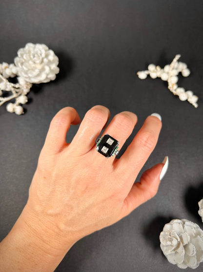 A geometric black onyx ring with diamonds and emeralds in white gold, modelled on a hand