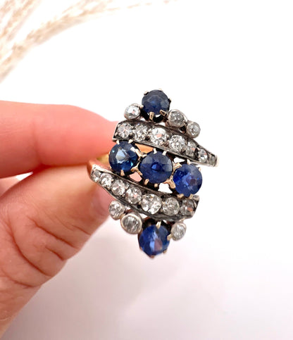 A navette shaped sapphire and diamond ring in yellow gold, held by a hand