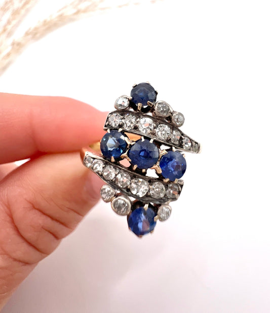 A navette shaped sapphire and diamond ring in yellow gold, held by a hand