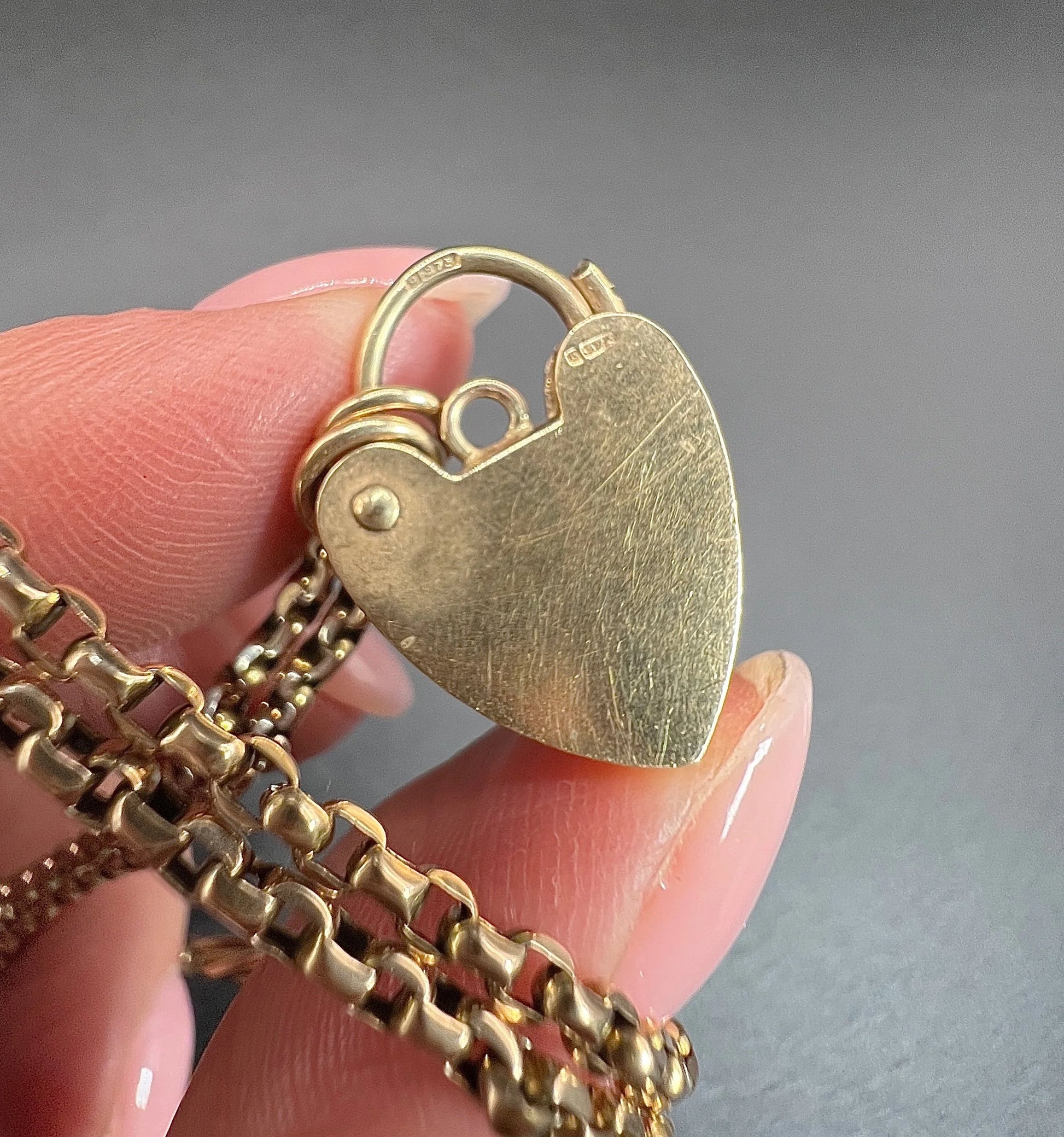 A yellow gold heart padlock, stamped, held in a hand