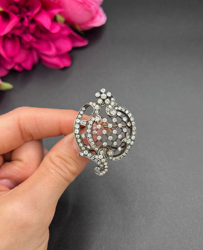 An openwork diamond set antique brooch in yellow gold and silver, held in a hand