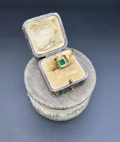 A square shaped emerald and diamond cluster ring in yellow and white gold, in a ring box