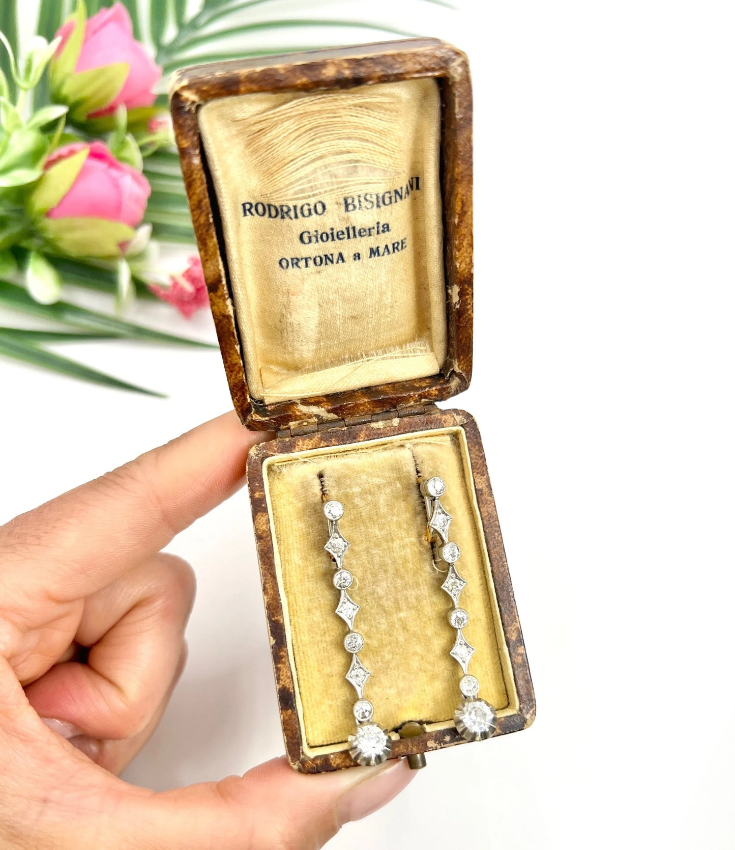 A pair of diamond drop earrings in yellow gold and platinum in an antique box, held in a hand