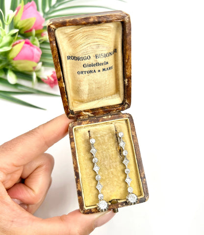 A pair of diamond drop earrings in yellow gold and platinum in an antique box, held in a hand