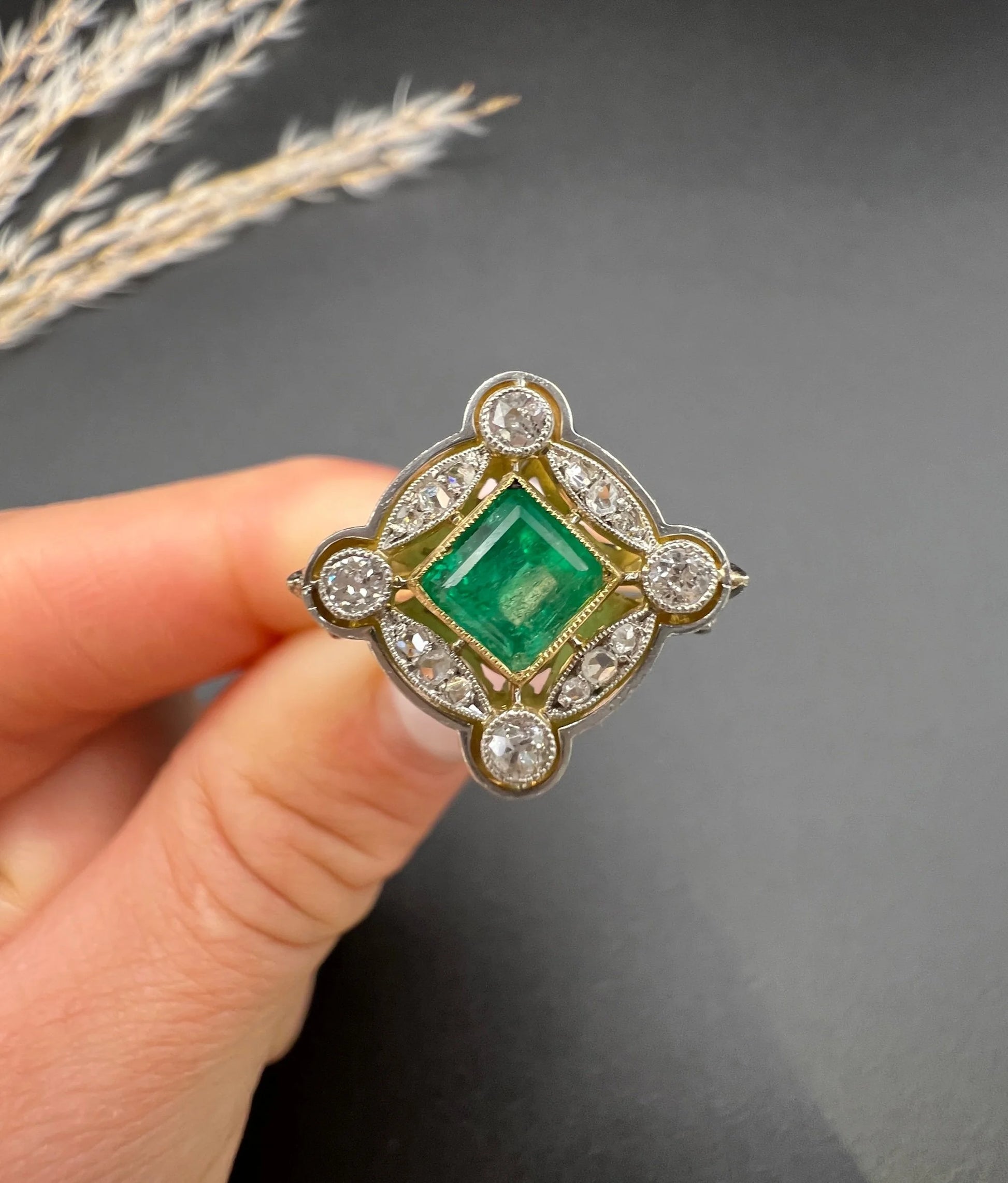 A gold and platinum ring with a centre emerald and diamond surround, held in a hand