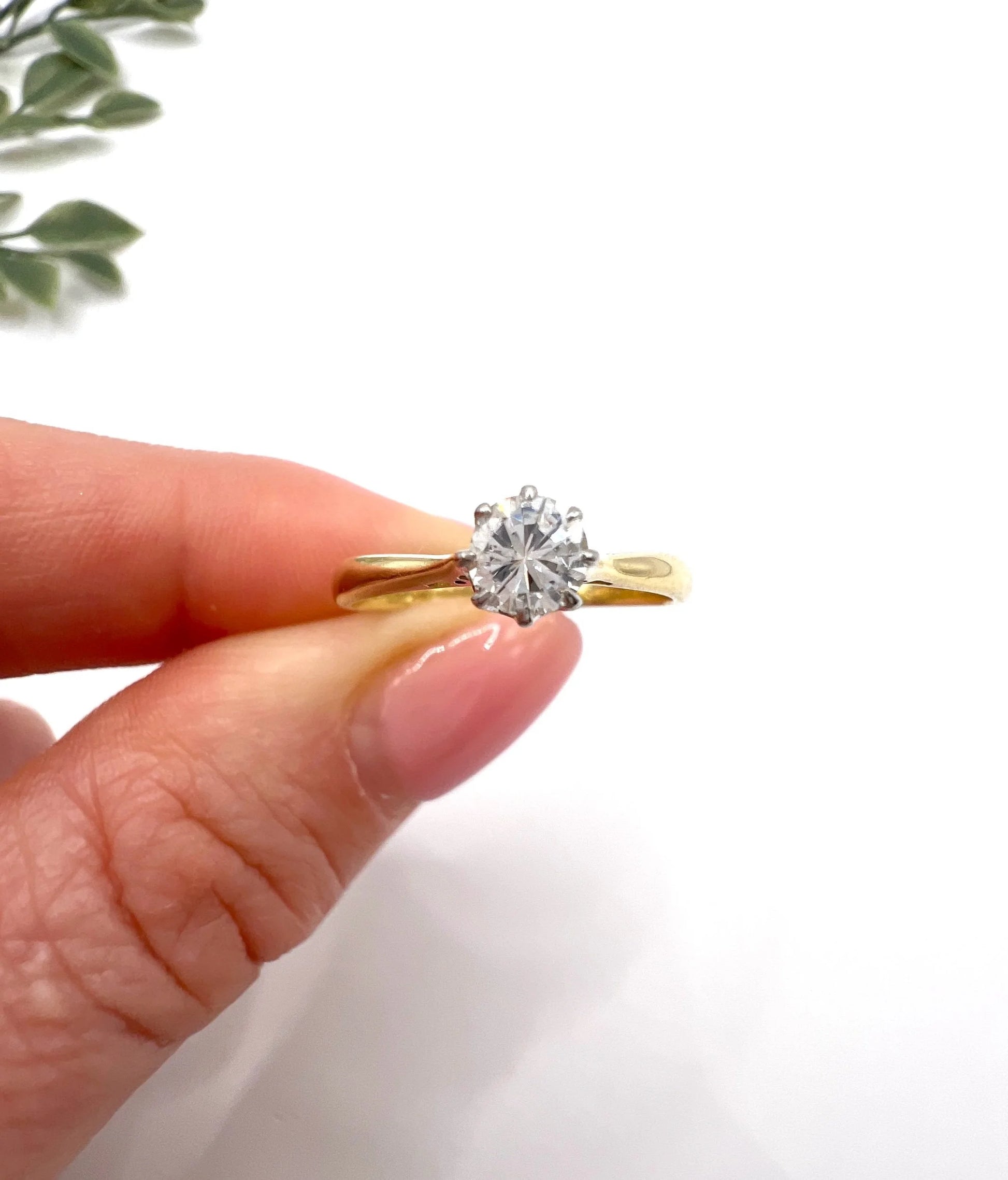 A single stone brilliant cut diamond ring claw set in platinum and yellow gold, held in a hand