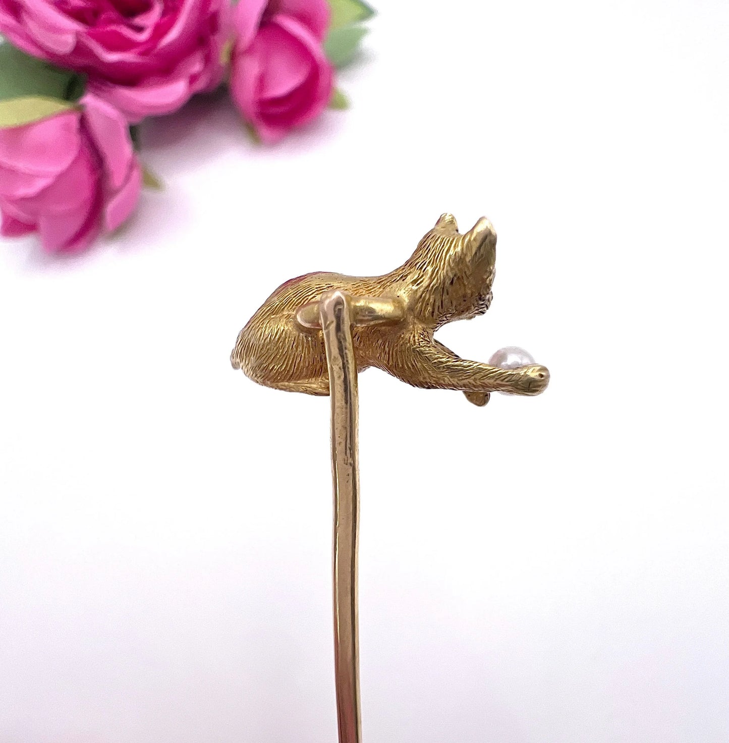 A yellow gold cat playing with a pearl ball stick pin