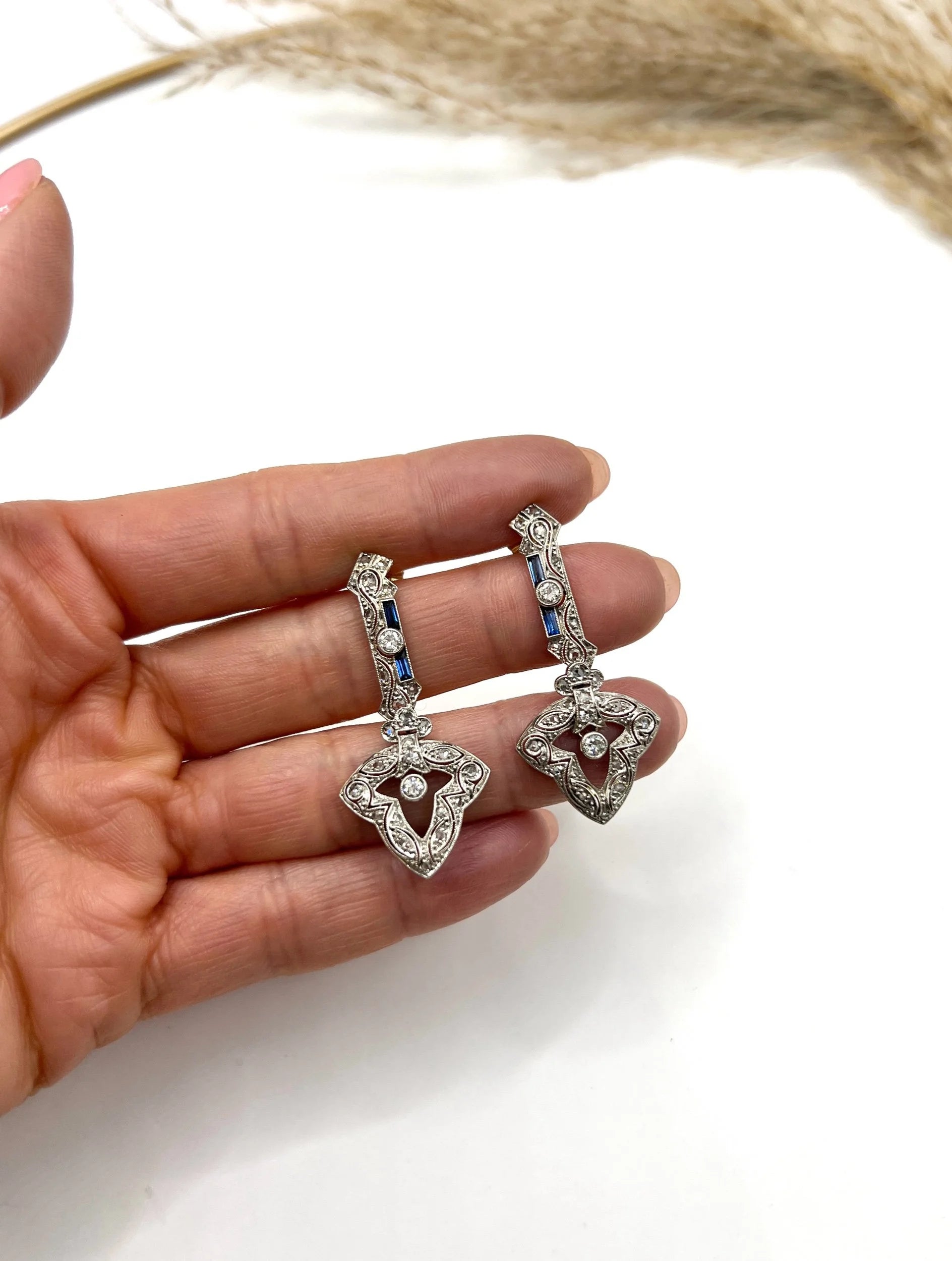 A pair of diamond and sapphire drop earrings, held in a hand