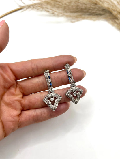 A pair of diamond and sapphire drop earrings, held in a hand