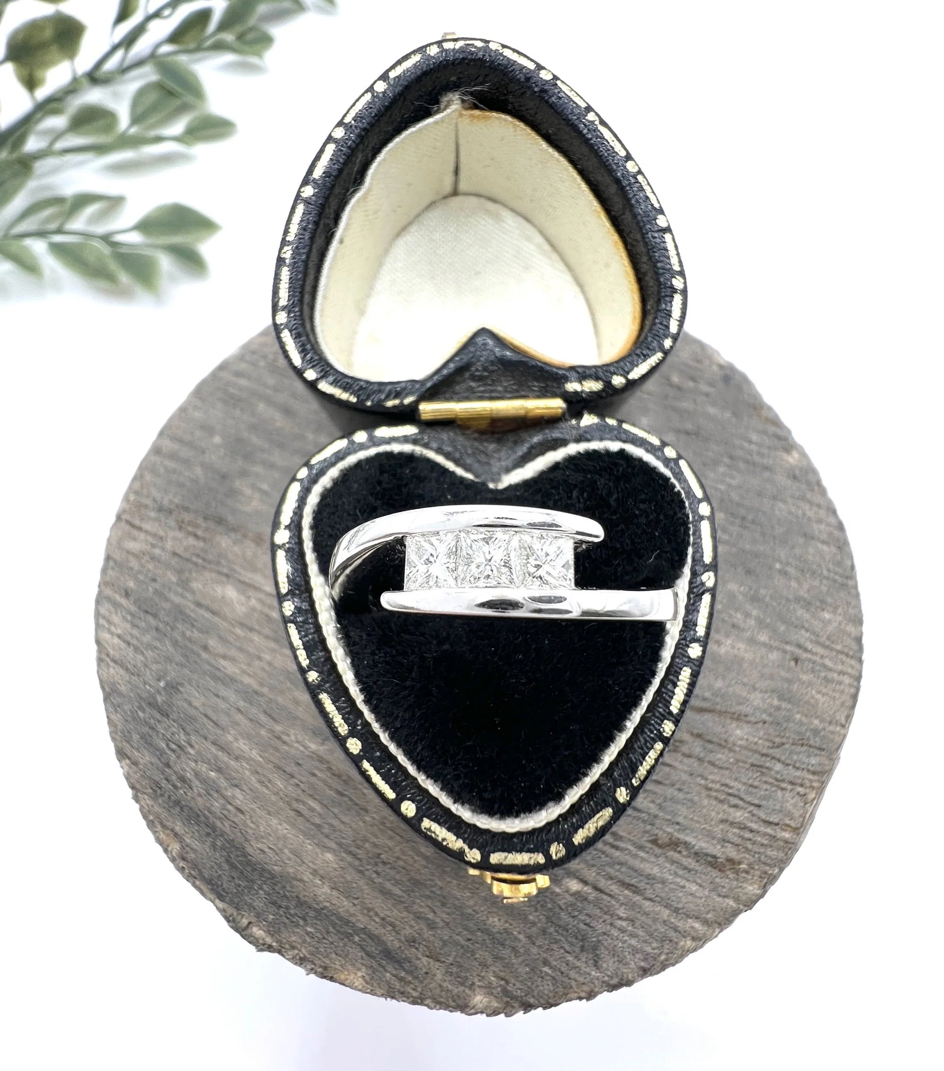 A three stone princess cut diamond crossover ring in white gold, in a heart-shaped ring box