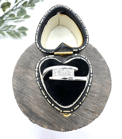 A three stone princess cut diamond crossover ring in white gold, in a heart-shaped ring box