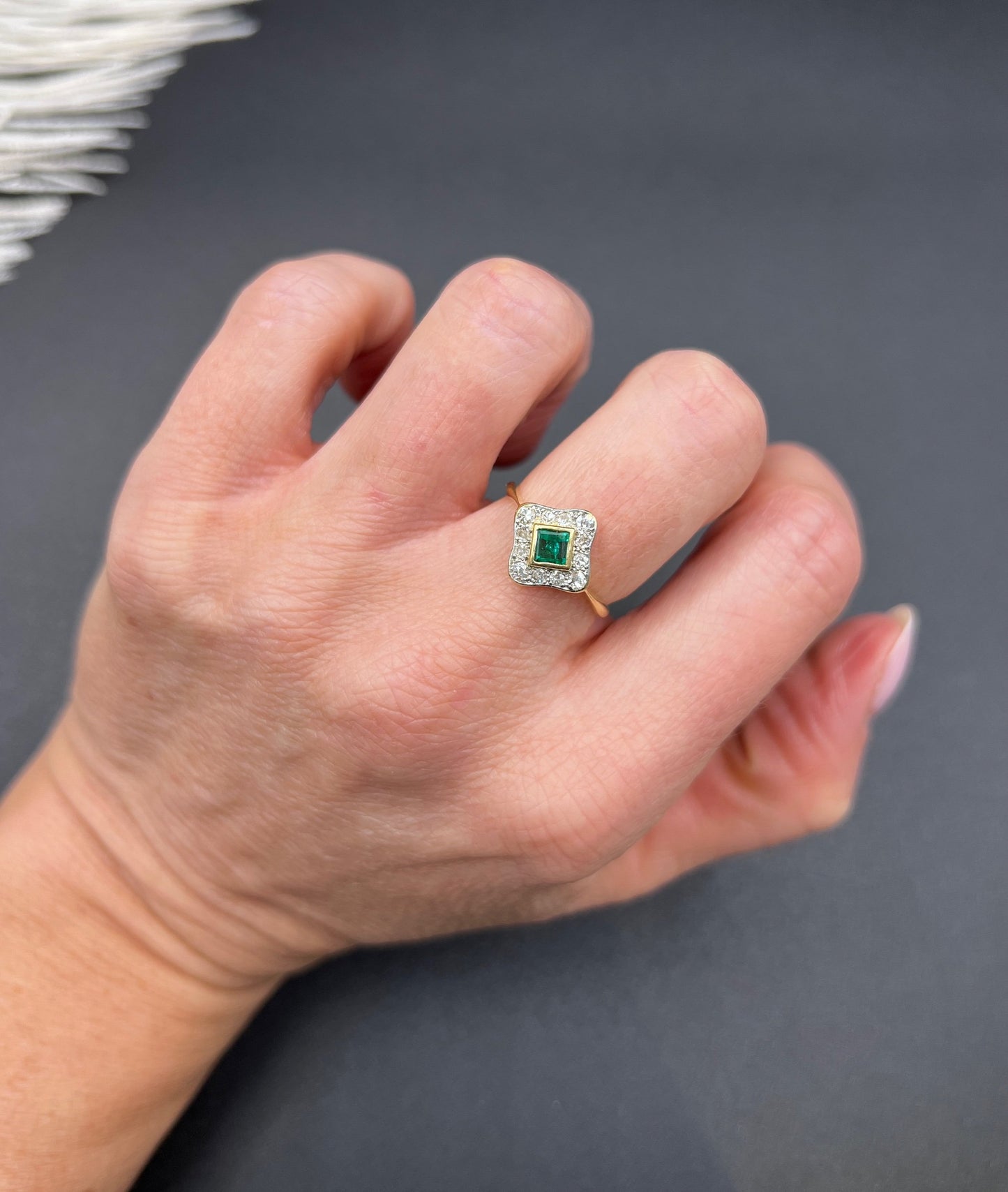 An emerald and diamond cluster ring in yellow gold and platinum, modelled on a hand