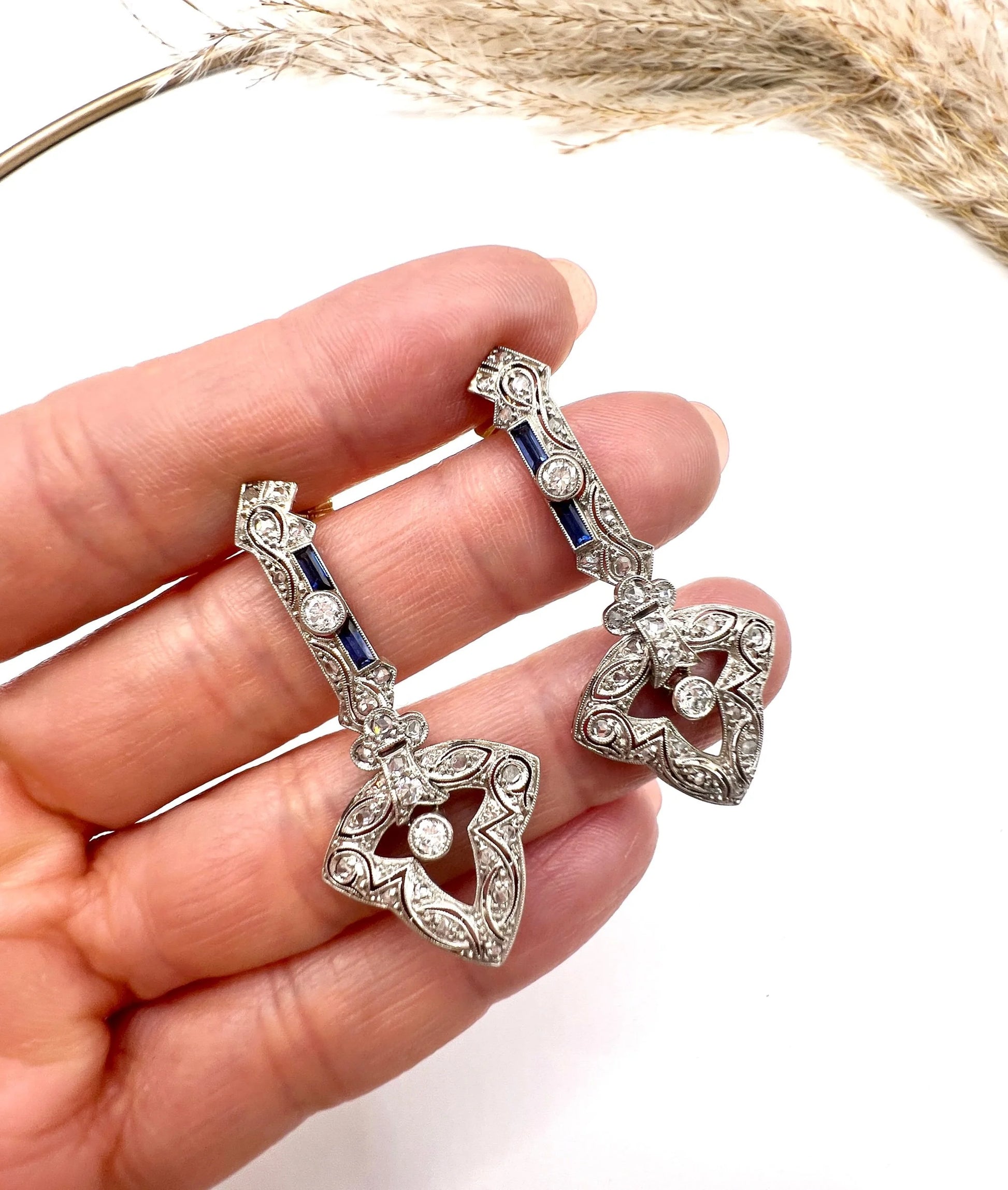 A pair of diamond and sapphire drop earrings, held in a hand