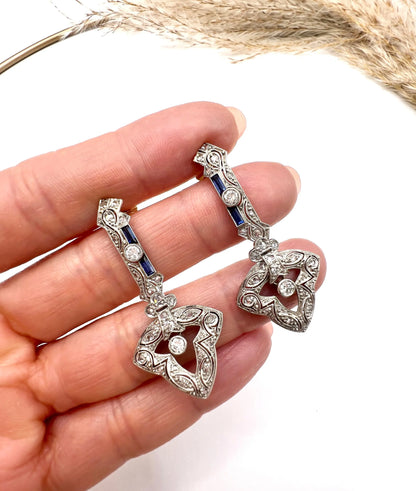 A pair of diamond and sapphire drop earrings, held in a hand