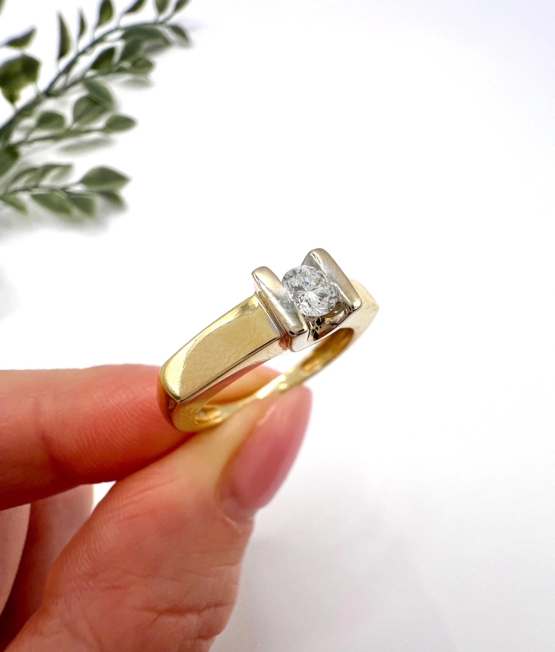 A brilliant cut diamond solitaire ring in yellow gold, held in a hand
