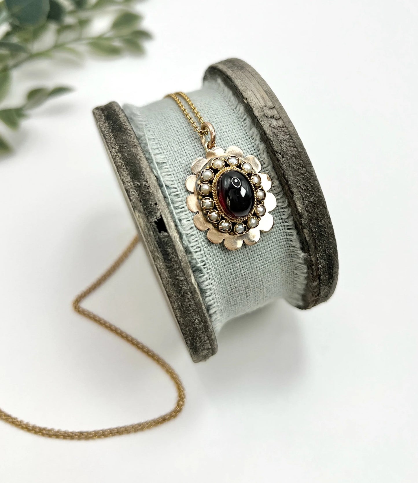 A cabochon garnet pendant with a seed pearl border in rose gold, with a chain
