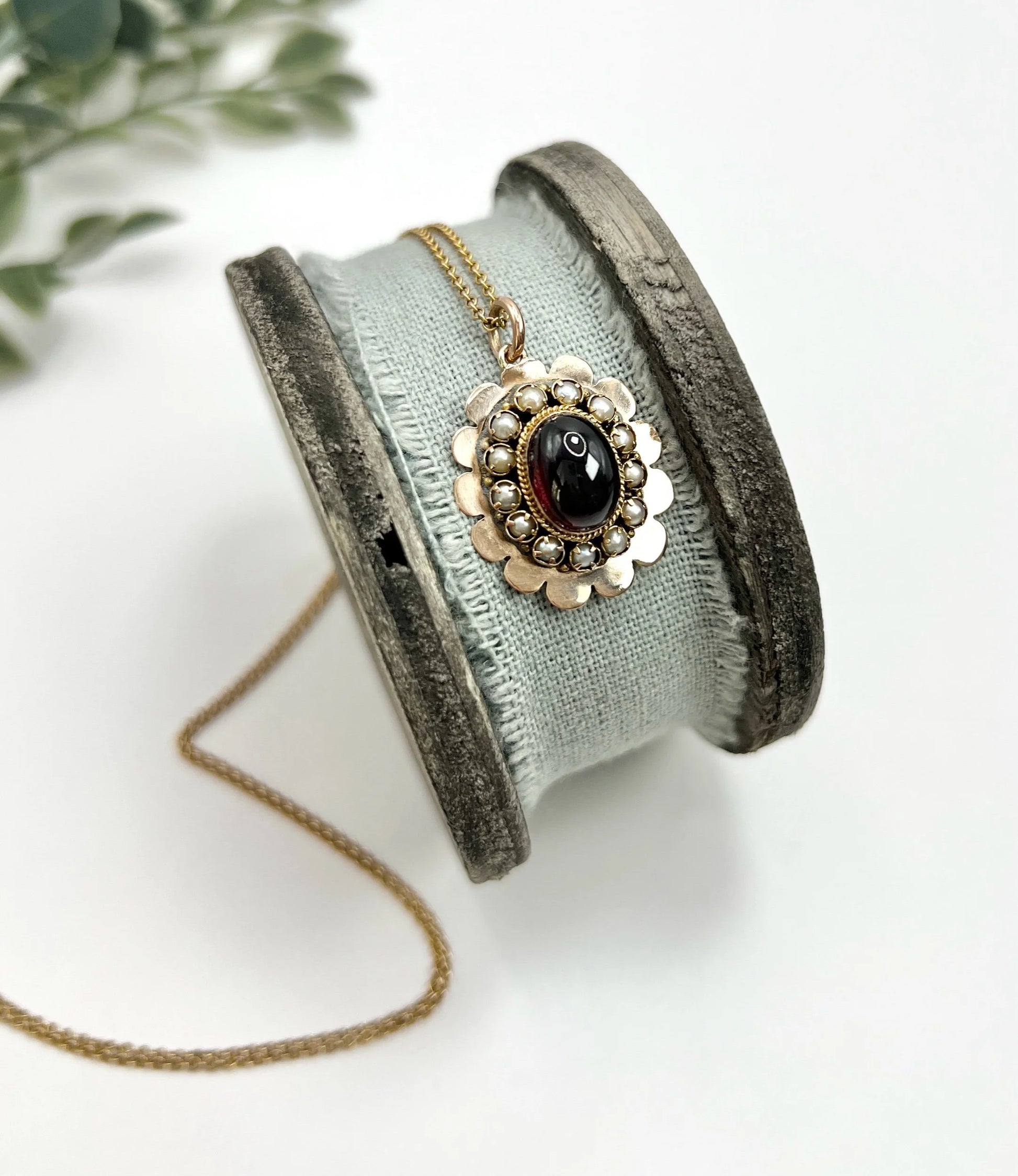 A cabochon garnet pendant with a seed pearl border in rose gold, with a chain