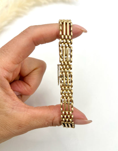 A yellow gold gate bracelet, held in a hand