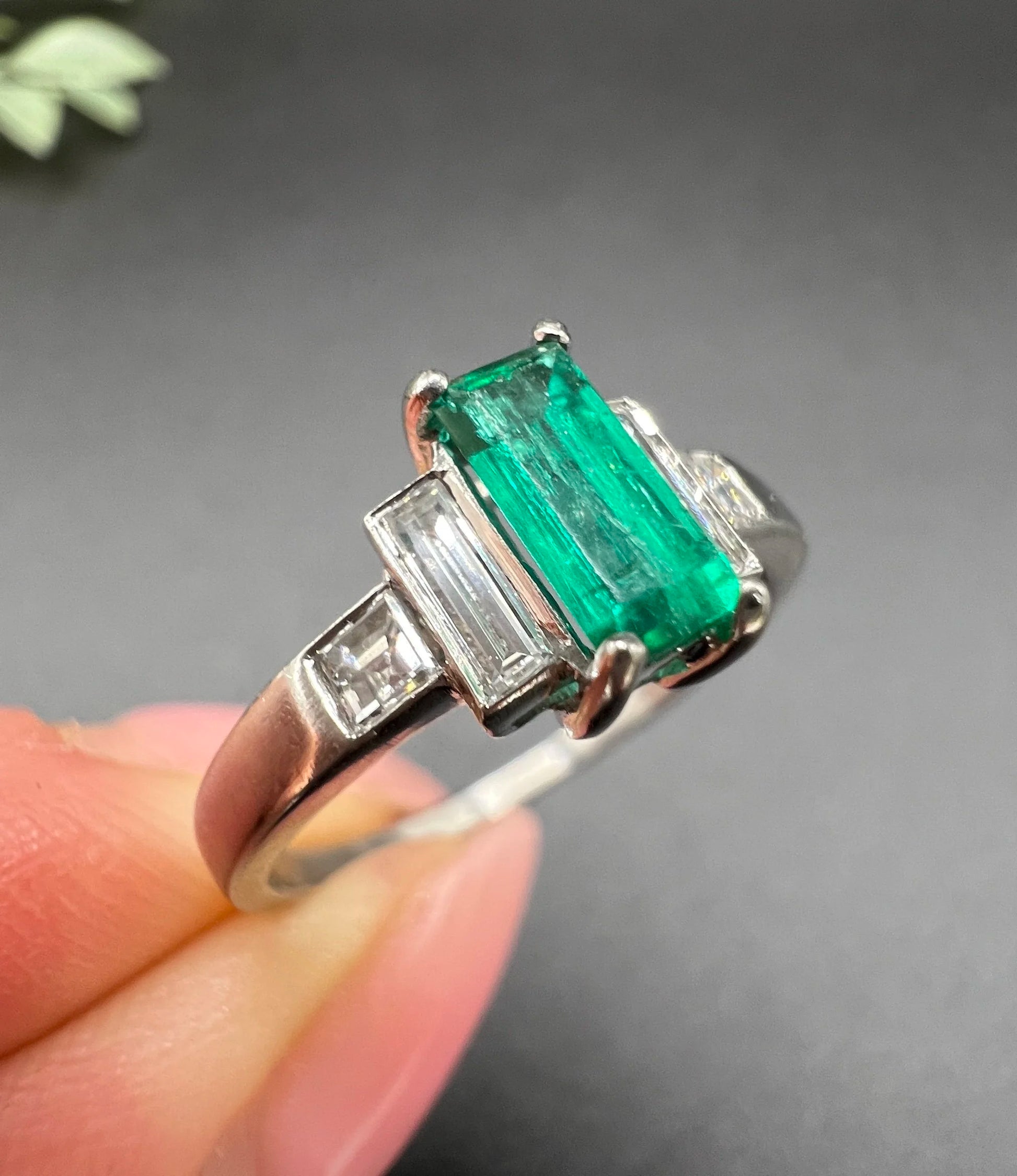 A five stone emerald cut emerald and baguette and square cut diamond ring in platinum, held in a hand