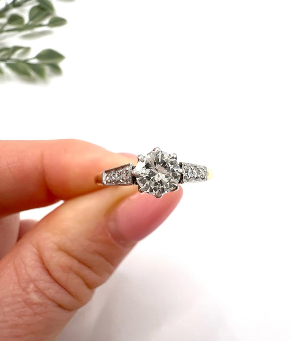 A diamond engagement style ring in yellow gold and platinum, held in a hand