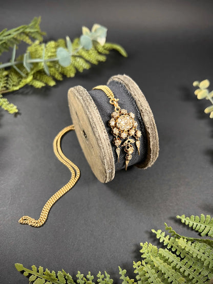 A yellow gold pendant with old cut diamonds, with a gold chain, on a wooden spool