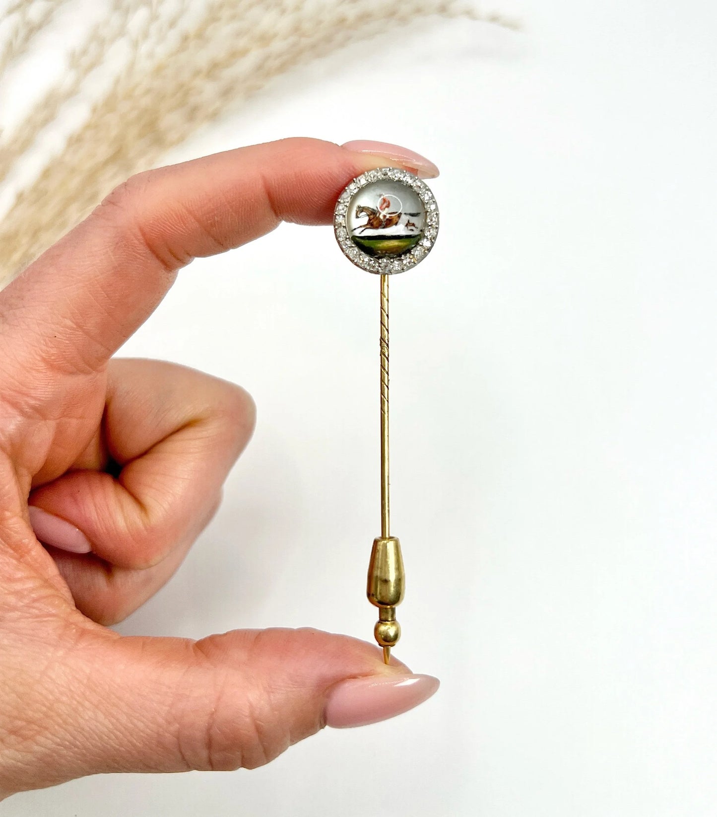 An antique Essex glass and diamond stick pin depicting a jockey riding a horse, in a hand