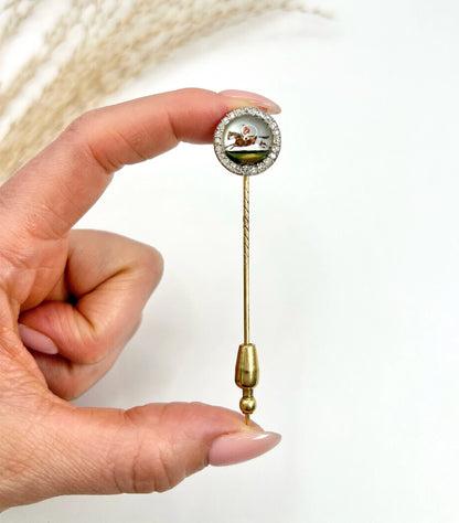 An antique Essex glass and diamond stick pin depicting a jockey riding a horse, in a hand