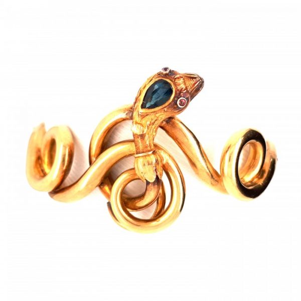 Antique Victorian Sapphire, Ruby and Gold Snake Bangle Bracelet; pear shape sapphire and cabochon ruby eyes set in a textured gold head with foliate design, on 18ct gold coiled body with a hinge and box and tongue clasp, Circa 1875