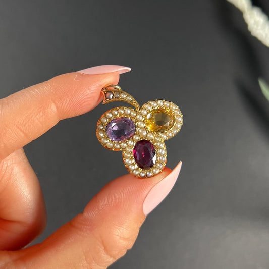 A yellow gold clover pendant with amethyst, citrine, garnet and seed pearls, held in a hand